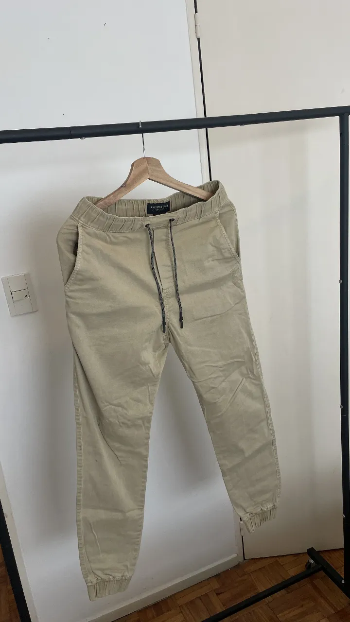 Pantalón de corte jogger de color beige, ideal para un look casual y cómodo. Cuenta con cordón ajustable en la cintura y puños elastizados en los tobillos. Presenta algunas manchas leves, como se observa en las fotos.