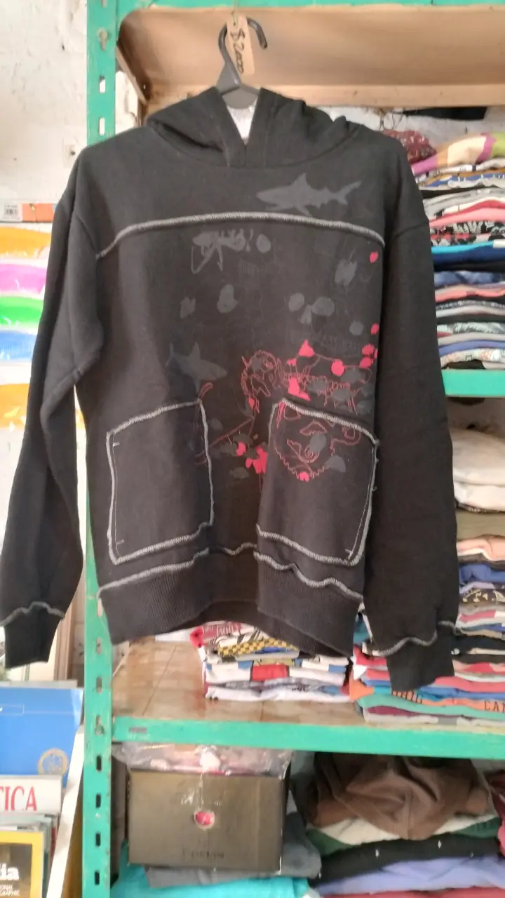 Buzo negro con capucha y detalles en gris. Estampado con diseños en rojo y gris. Bolsillos delanteros.
