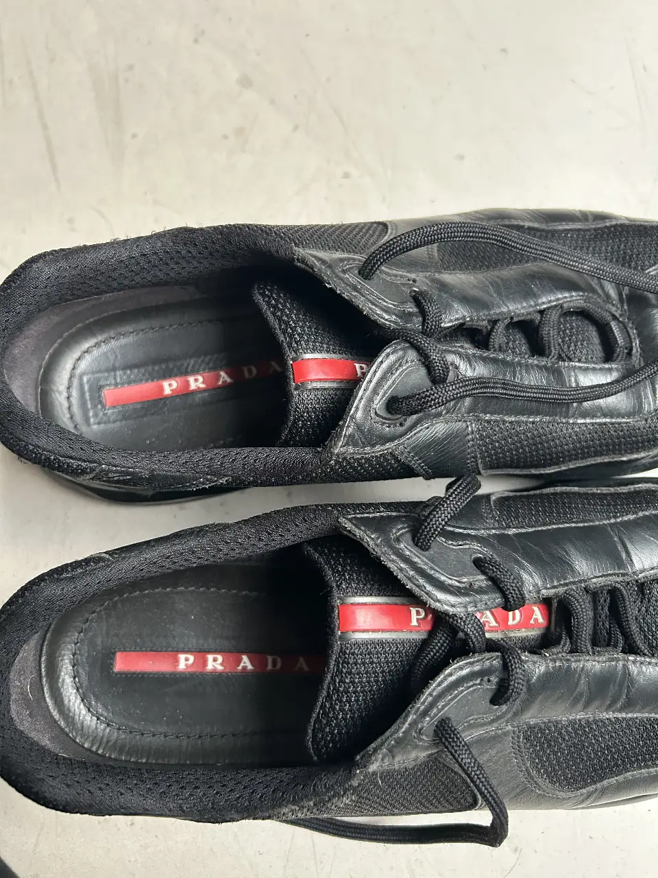 Zapatillas Prada de cuero negro para hombre. Diseño clásico con detalles de malla y suela de goma. Ideales para un look casual y moderno.