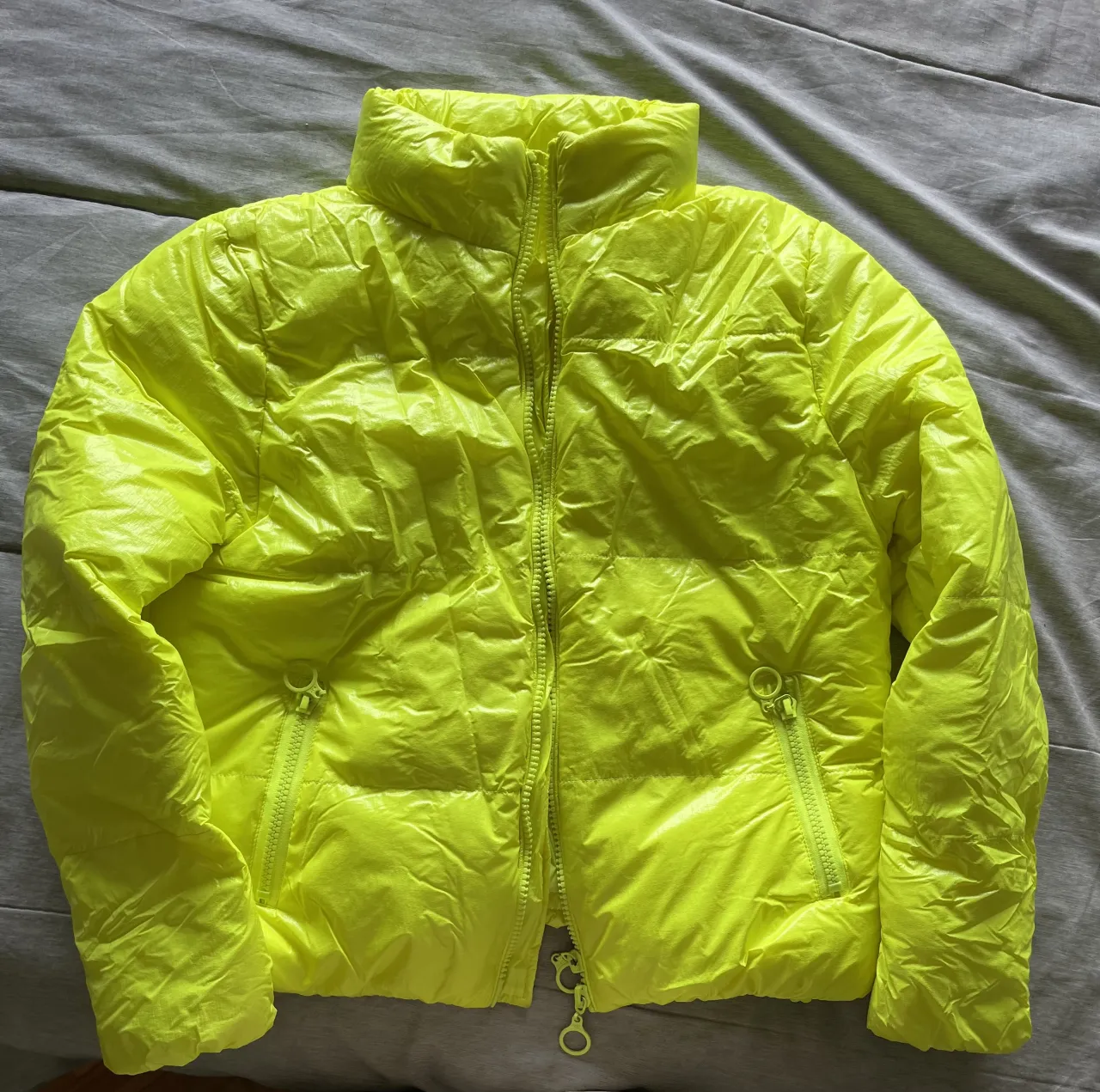 Campera acolchada color amarillo flúo. Tiene cierre al frente y bolsillos laterales con cierre. Incluye una bolsa para guardarla.