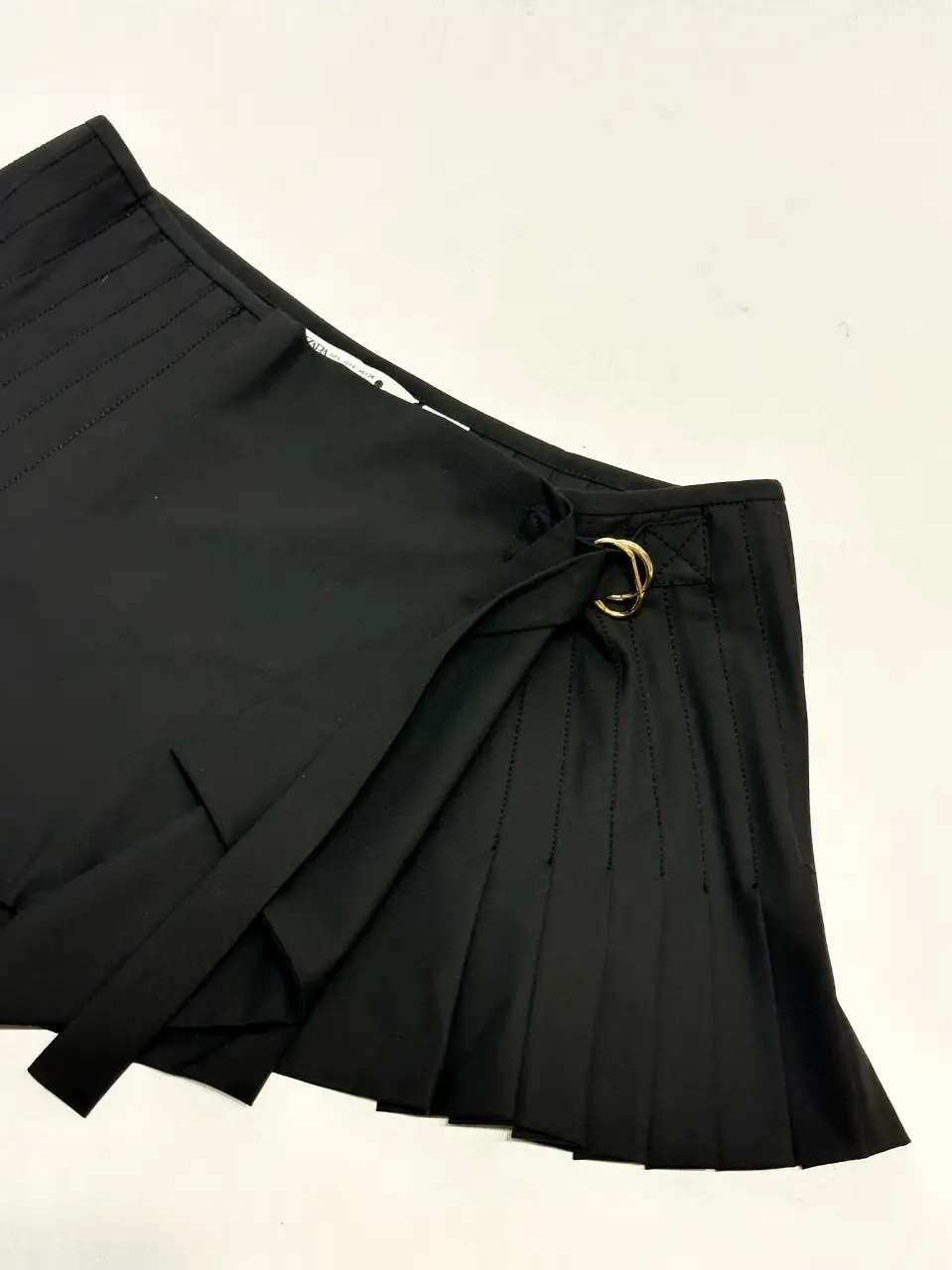 Pollera sastrera negra de ZARA con detalles de diseño. Corte asimétrico con pliegues y un aro dorado como detalle. Ideal para un look elegante y moderno.