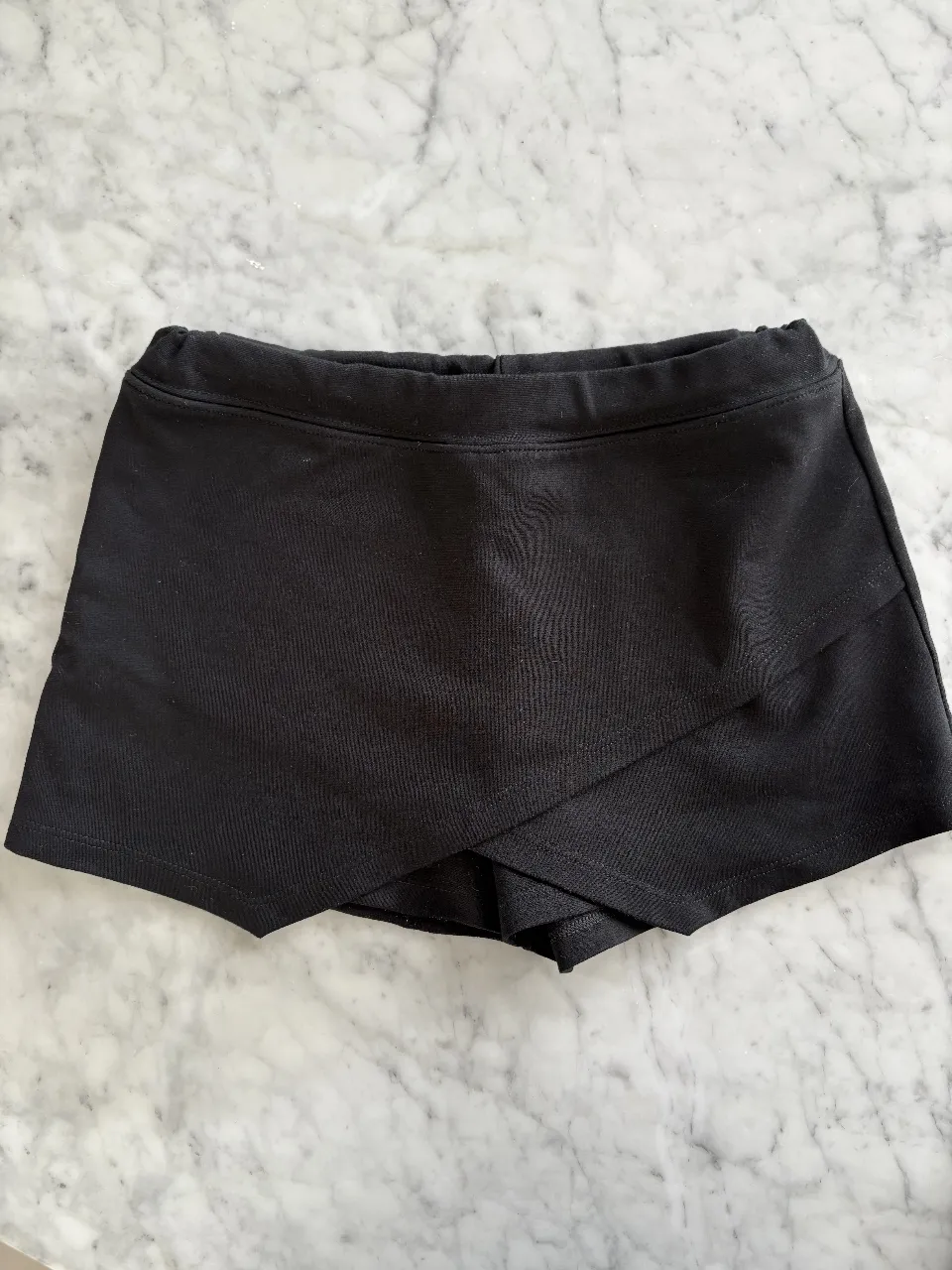 Shorts pollera negros, para un look casual y cómodo. Tienen un diseño cruzado al frente que le da un toque moderno y femenino. Perfectos para combinar con remeras o tops.