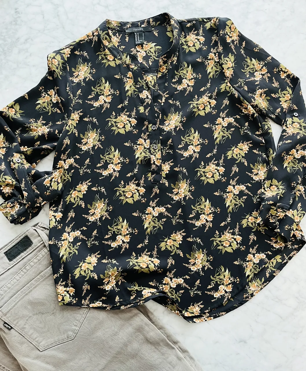Blusa negra con estampado floral en tonos ocres y verdes. Posee cuello mao con tajito y botones al frente. Mangas largas con puño y botón. Ideal para un look casual y femenino.