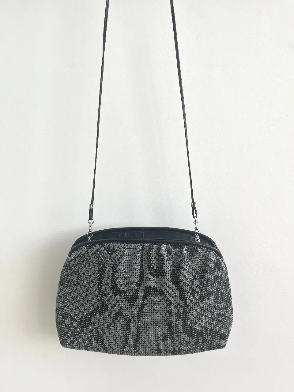 Cartera de fiesta plateada con diseño de escamas y detalles en cuero negro. Ideal para complementar tu look en eventos especiales. Su tamaño es perfecto para llevar lo esencial.