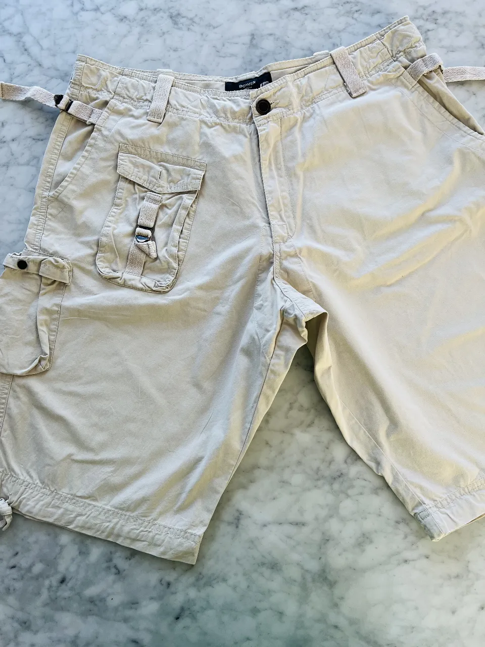 Shorts de gabardina color tiza, estilo cargo con múltiples bolsillos funcionales y detalles de ajuste con hebillas y tiras. Perfectos para un look casual y cómodo.
