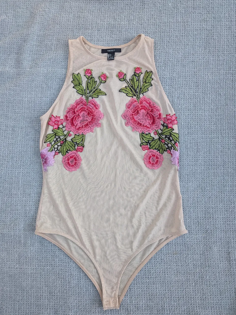 Body de red con bordados de flores rosas y hojas verdes en el busto. Escote redondo y sin mangas.