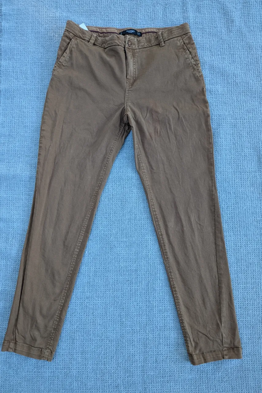 Pantalón de gabardina color marrón claro con bolsillos delanteros y traseros. Cierre y botón en la parte frontal. Detalle de botón en uno de los bolsillos traseros.