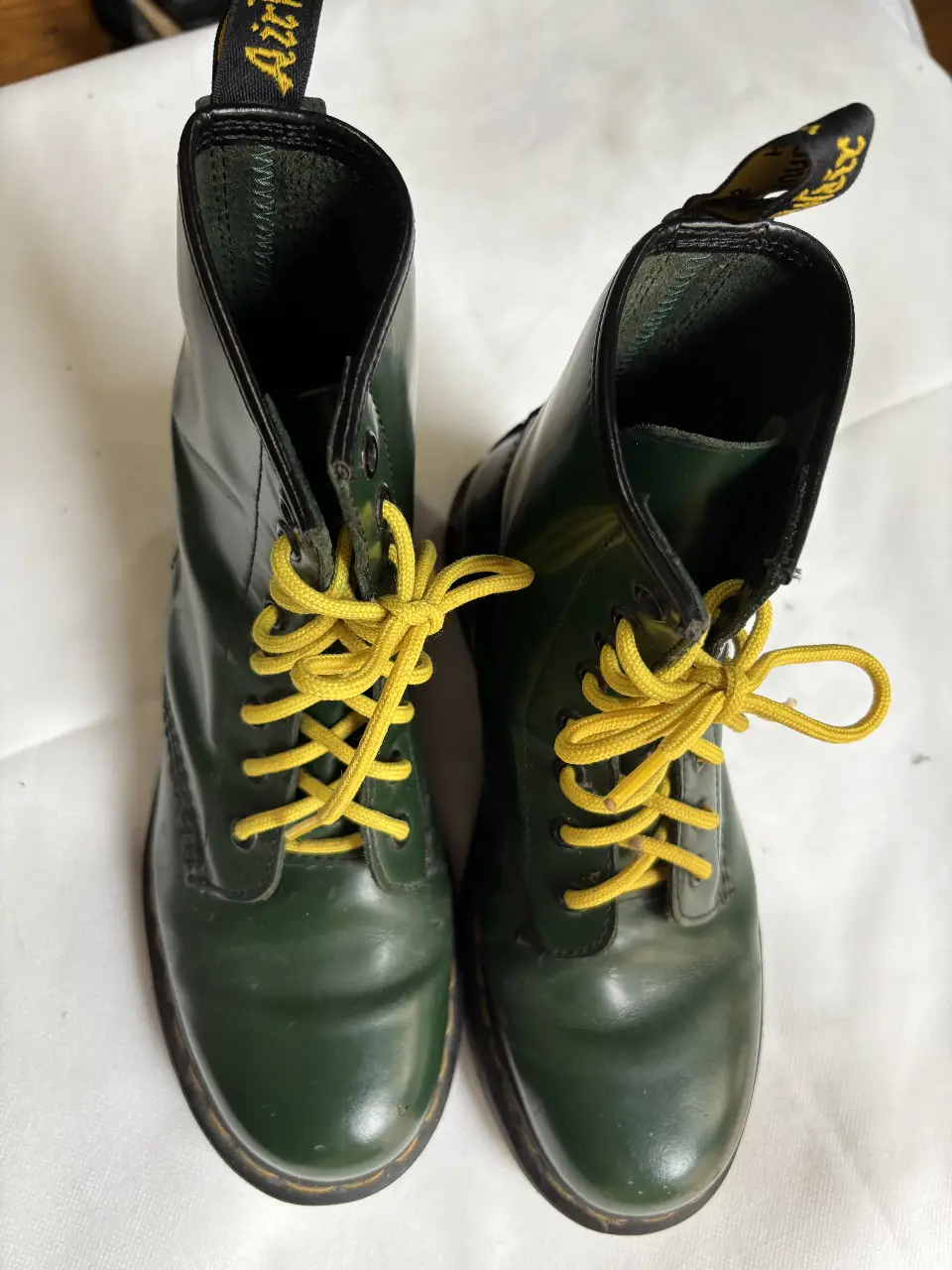 Borcegos Dr. Martens verdes con cordones amarillos. Estilo clásico y duradero, ideales para un look urbano y con personalidad.