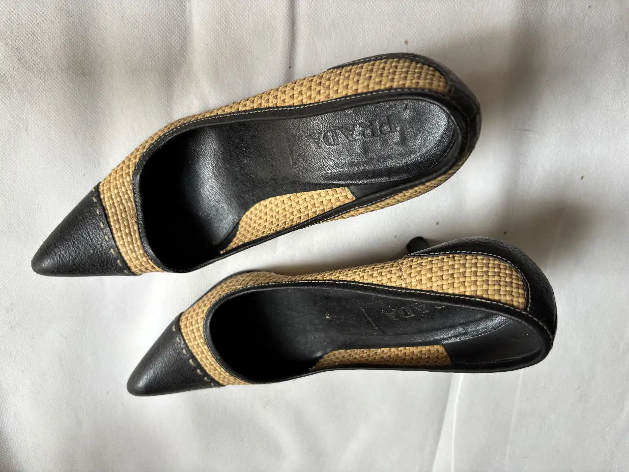 Elegantes zapatos de taco alto PRADA, combinando cuero negro con detalles en rafia color crudo. Ideales para una ocasión especial.