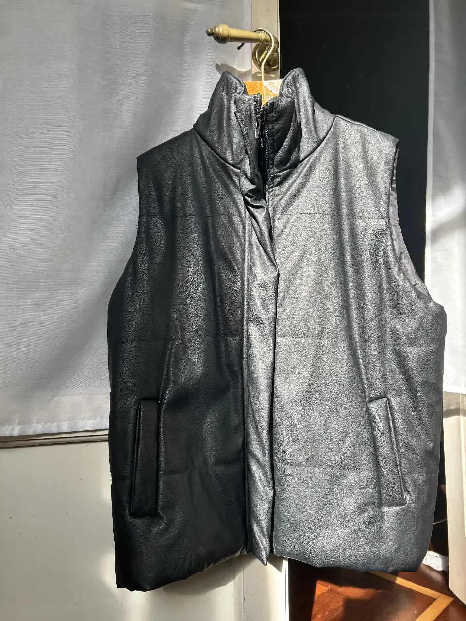 Chaleco acolchado de cuero sintético negro, con cuello alto y cierre. Ideal para un look moderno y abrigado.