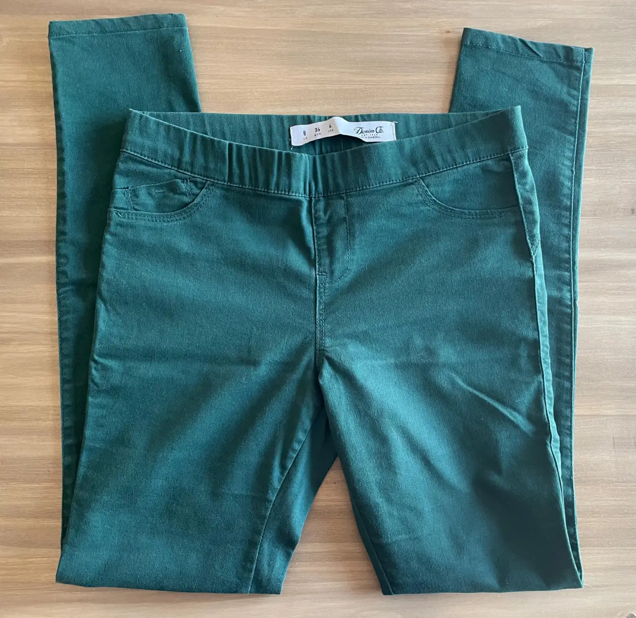 Pantalón tipo chupín de color verde oscuro, con cintura elastizada y bolsillos delanteros. Ideal para un look casual y cómodo.Talle 8 UK, 36 EUR, 4 USA. Marca Denim Co. 36 cm cintura, 40 cm cadera, 97 cm largo.