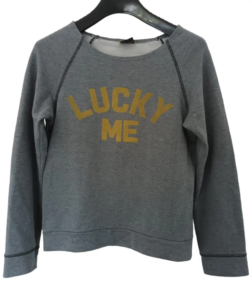 Buzo de cuello redondo gris con estampado "LUCKY ME" en amarillo. Ideal para un look casual y cómodo.