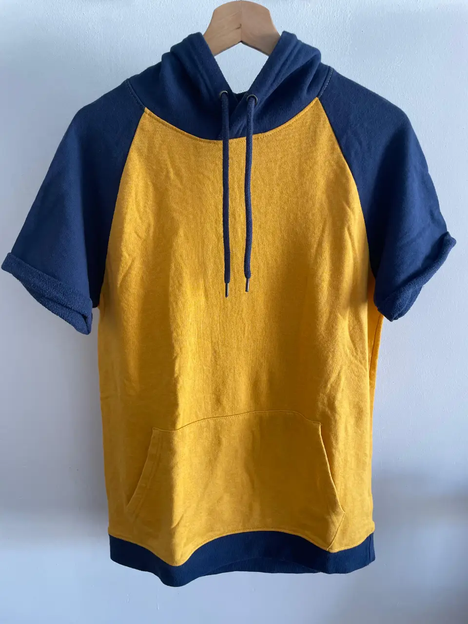 Buzo deportivo con capucha y mangas cortas, de color amarillo con detalles en azul marino. Ideal para un look casual y cómodo. Sisa 52 cm, largo  71 cm.