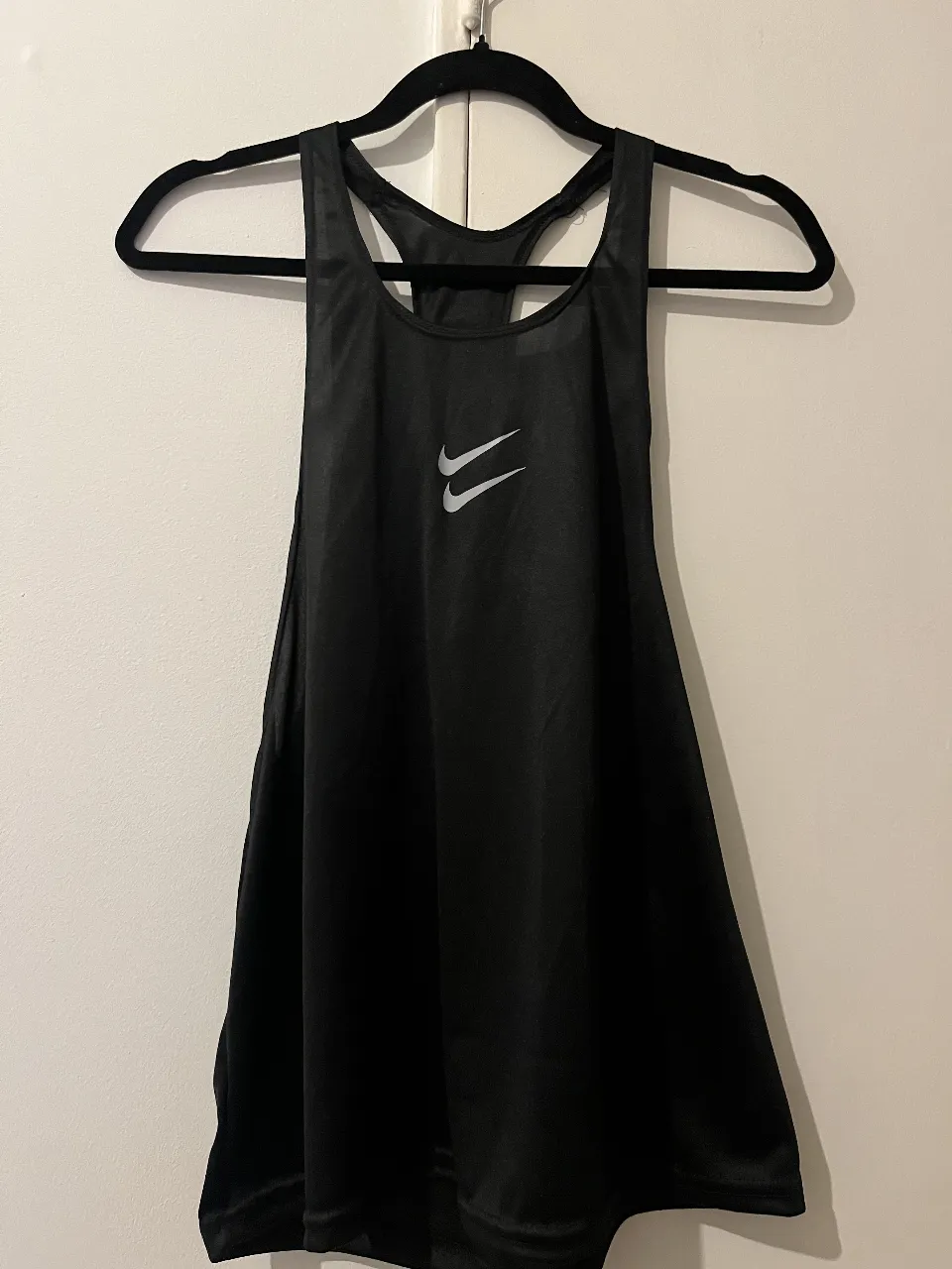 Musculosa deportiva Nike negra, ideal para entrenamientos intensos. Diseño moderno con logo plateado y estampa "JUST DO IT." en la espalda.