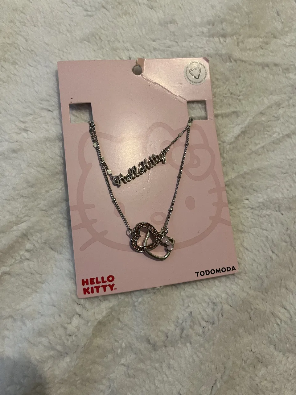 Conjunto de collar y pulsera de Hello Kitty. El collar tiene la inscripción "Hello Kitty" y un dije doble de corazones con brillos y el moño característico. La pulsera es delicada y combina con el collar. Ideal para fans de Hello Kitty.