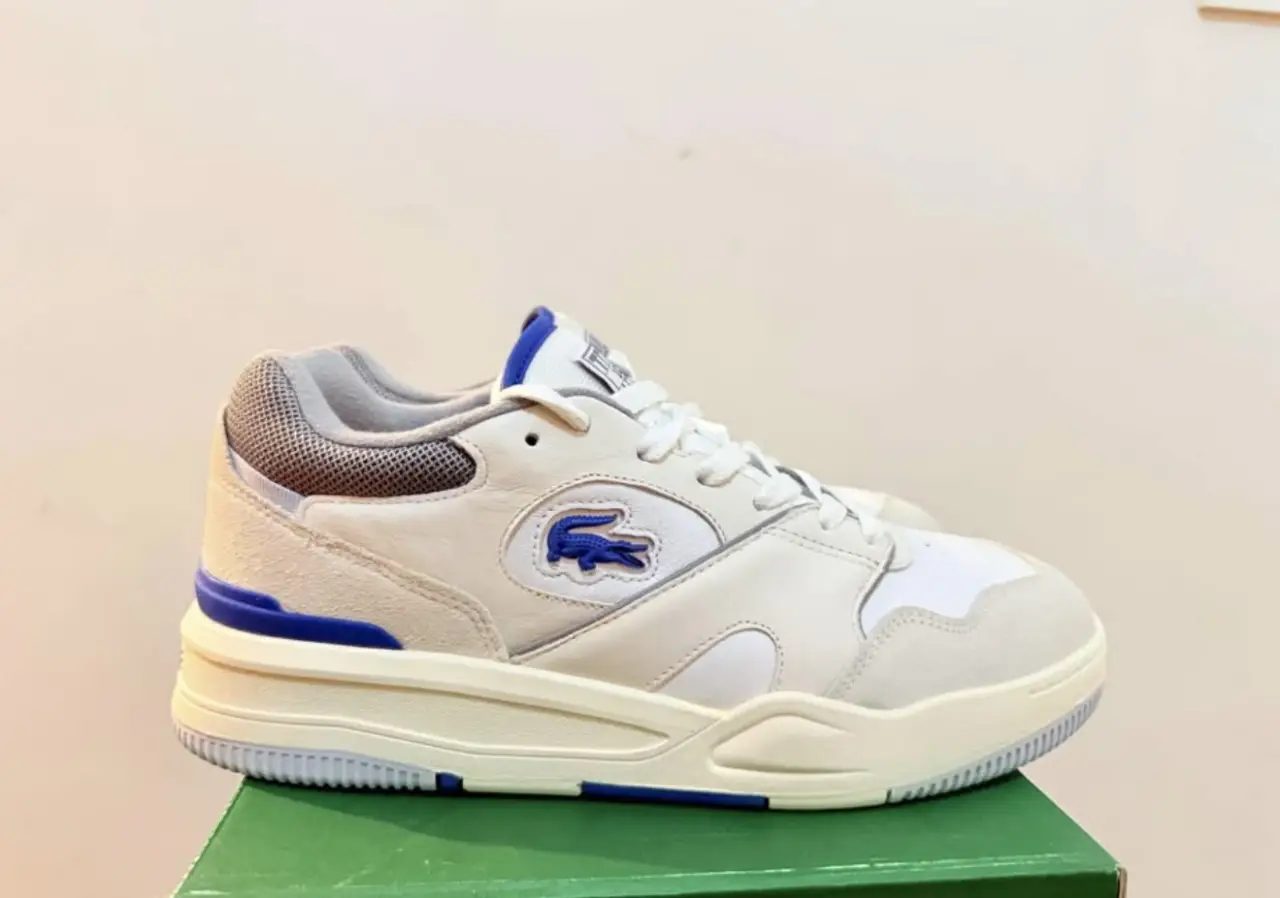 Zapatillas Lacoste Lineshot 124 1, blancas con detalles en azul y gris. Diseño deportivo y moderno, ideales para un look casual y cómodo. Con logo de la marca en el lateral y detalles de diseño en la suela.