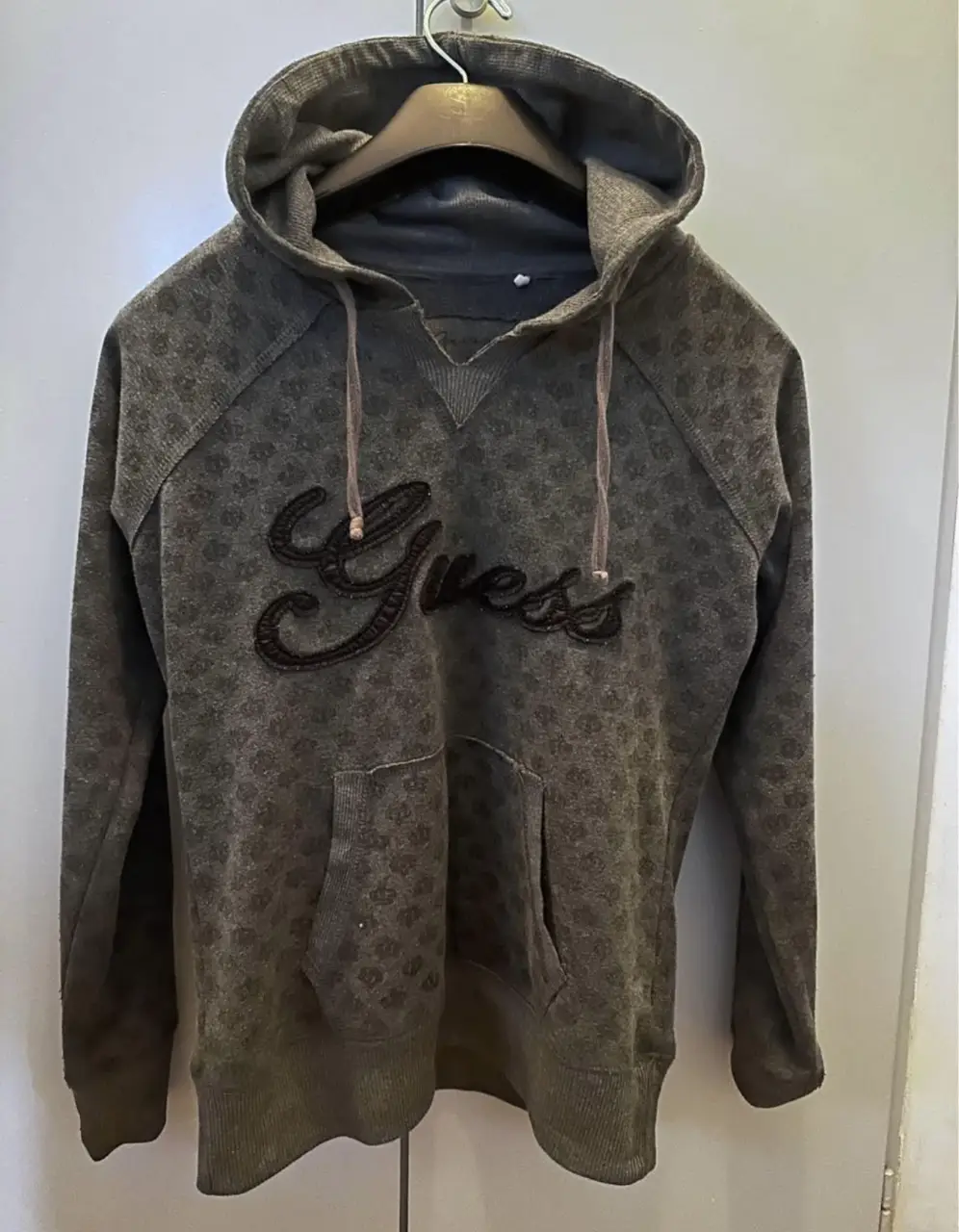 Buzo canguro Guess gris con estampado de coronas y el logo de la marca en relieve. Ideal para un look casual y cómodo. Original.