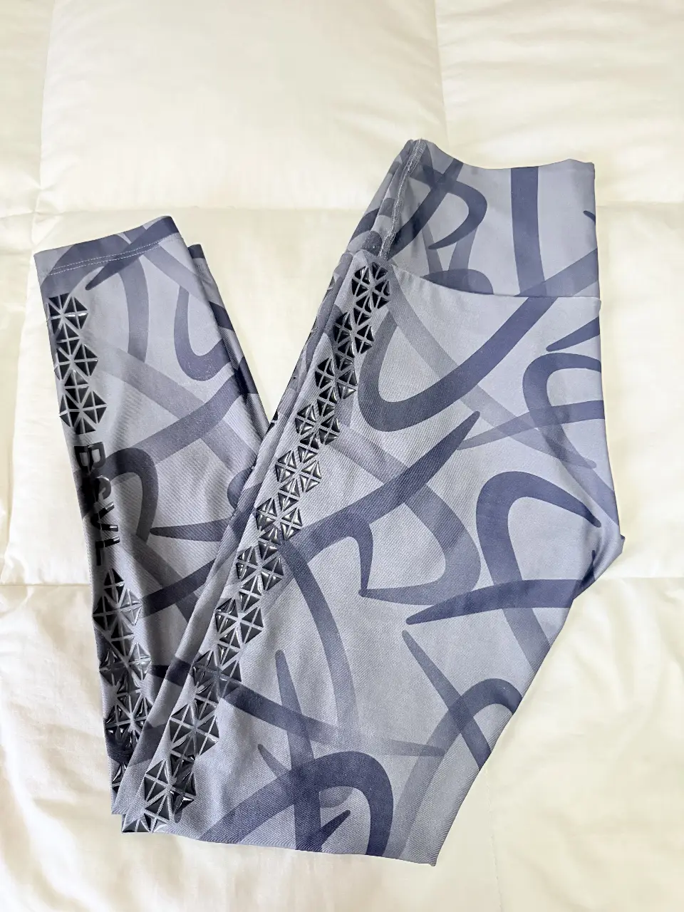 Calzas deportivas grises con estampado abstracto y detalles geométricos en los laterales. Ideal para entrenamientos y actividades físicas.
