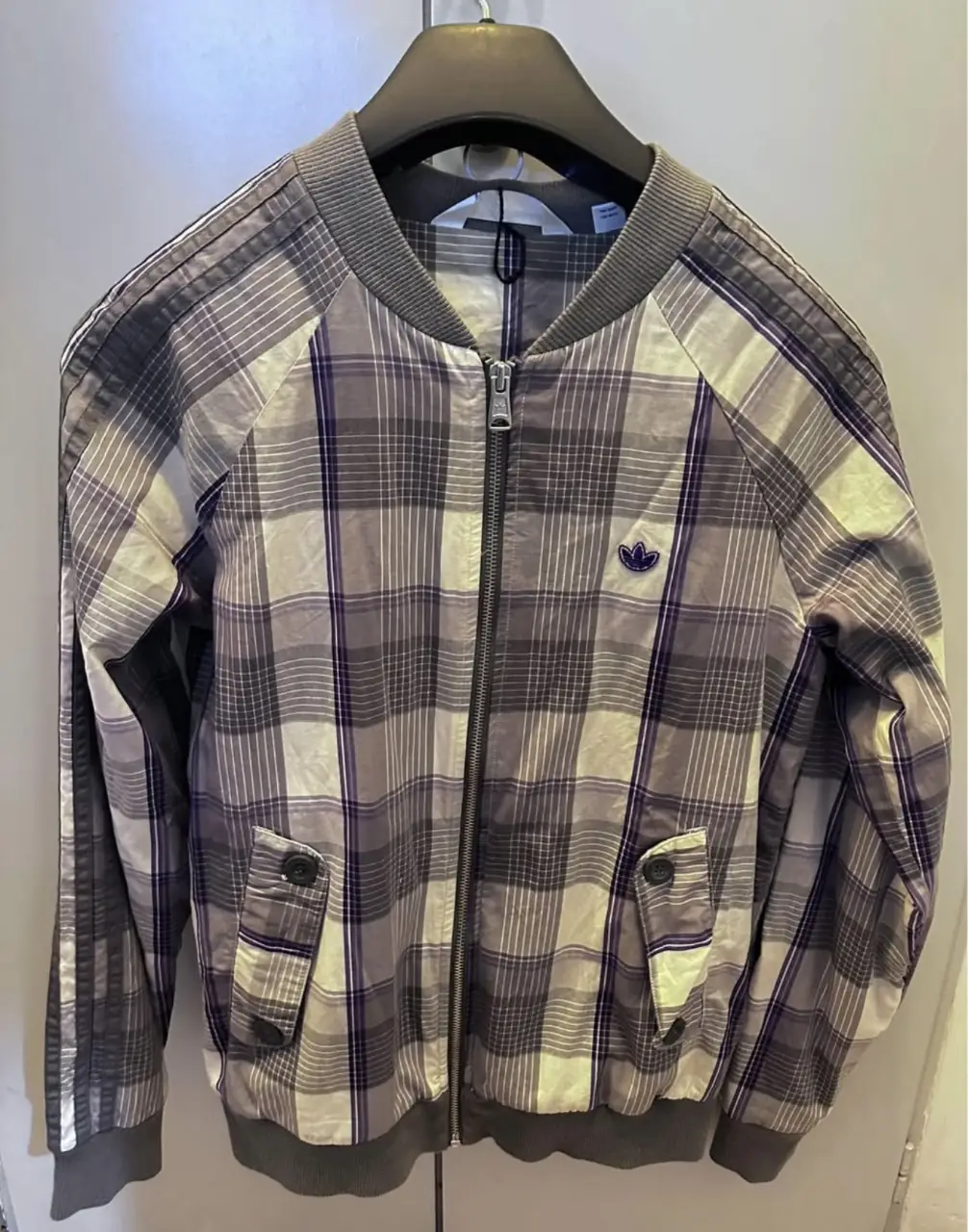 Campera Adidas bomber con estampado a cuadros en tonos grises y violetas. Con cierre frontal, bolsillos y el logo de la marca bordado. Ideal para un look casual y urbano. original 