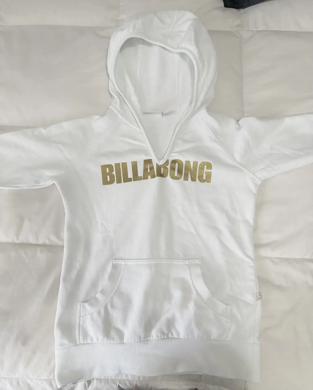 Buzo canguro blanco de la marca Billabong con estampado dorado. Ideal para un look casual y cómodo.