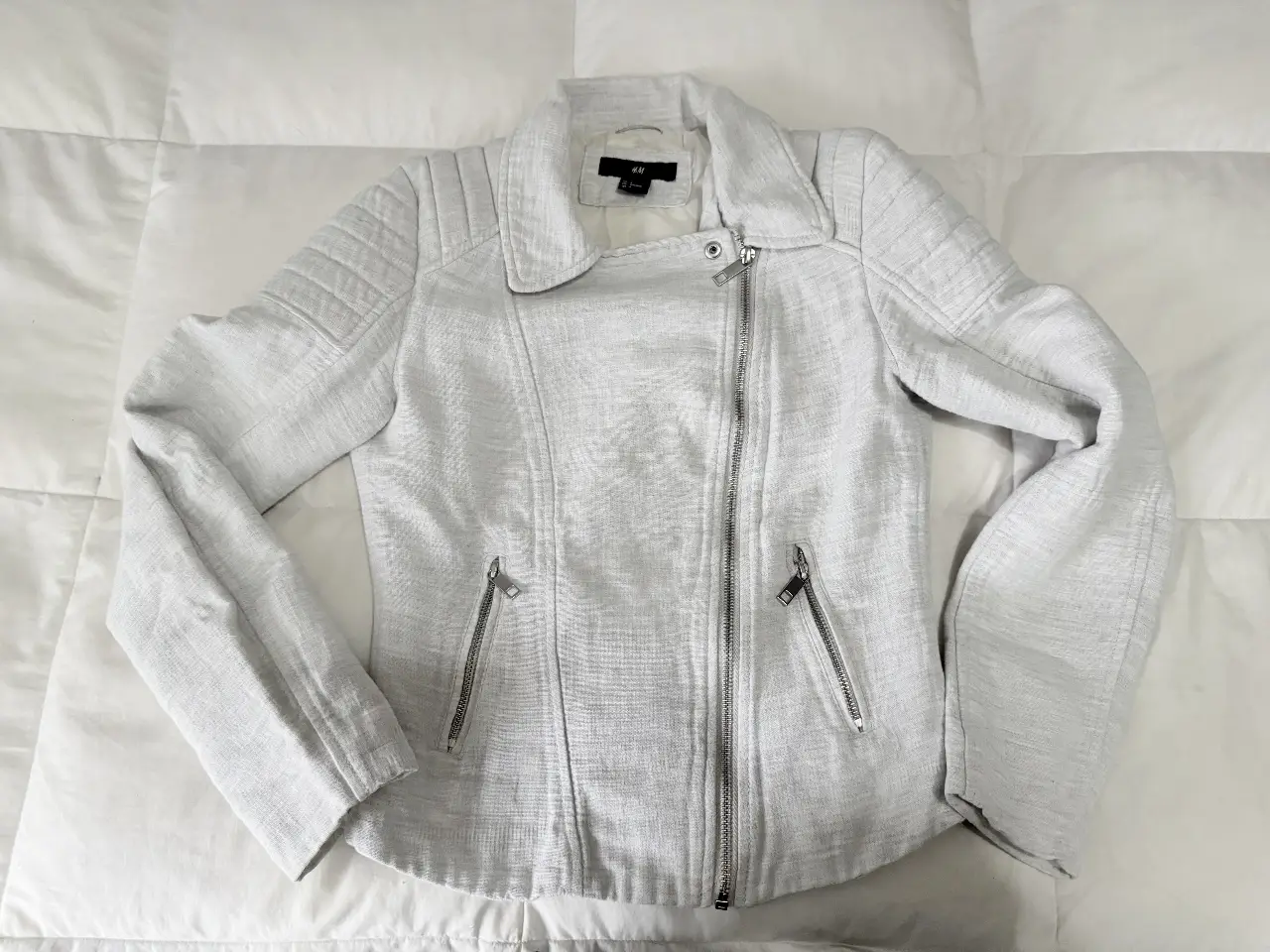 Campera estilo biker de mujer, color blanco, con cierre asimétrico y detalles en los hombros. Talle 4, de la marca H&M.