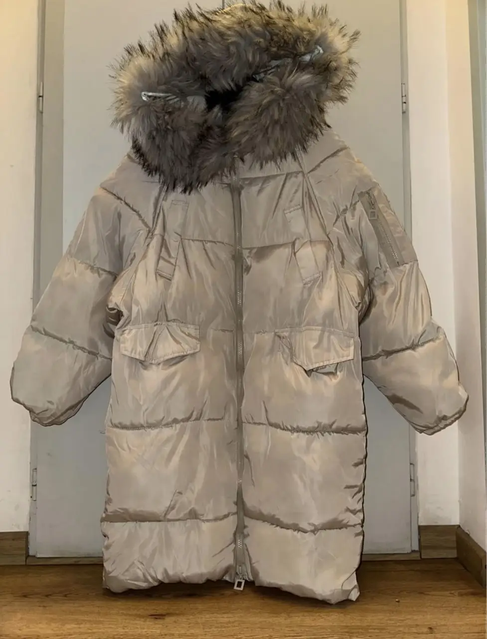 Campera larga acolchada para mujer, color crudo con capucha y borde de piel sintética. Posee bolsillos delanteros y cierre frontal. Ideal para el invierno. importada 