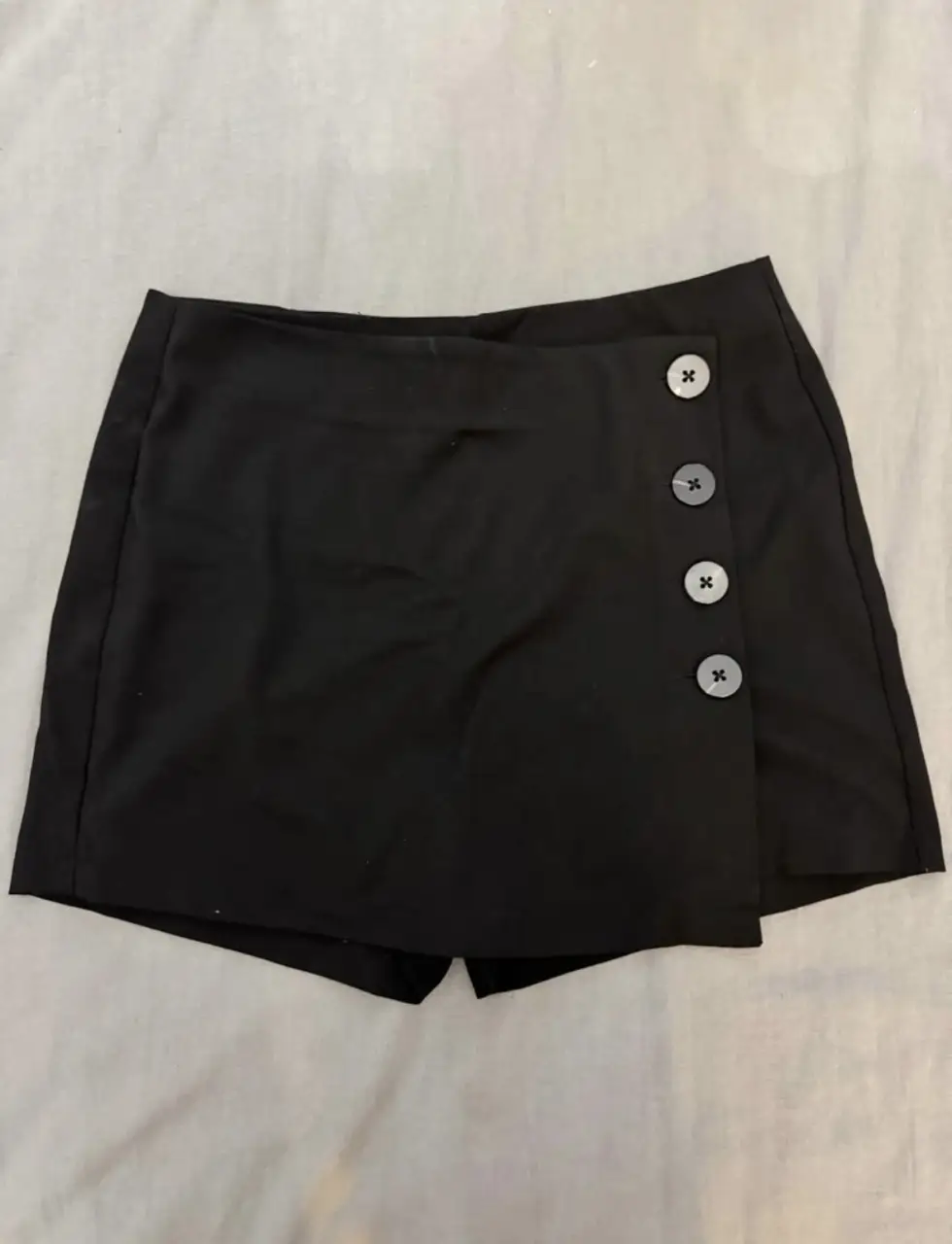 Short negro con diseño de falda pantalón y botones decorativos. Ideal para un look moderno y versátil.