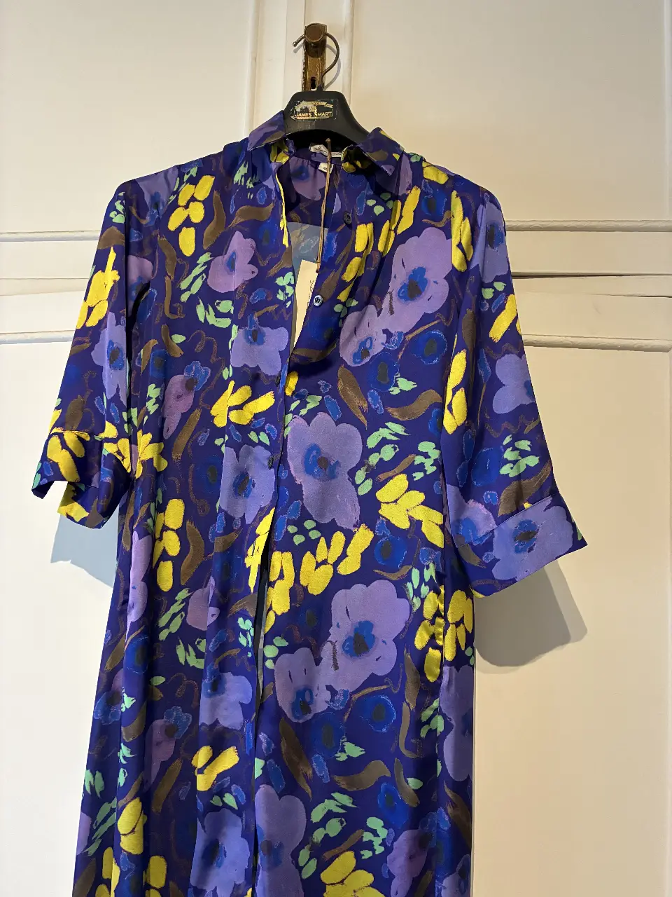 Vestido midi de seda con estampado floral en tonos azules, amarillos y violetas. Diseño con cuello camisero, botones frontales y mangas cortas. Ideal para un look elegante y fresco.