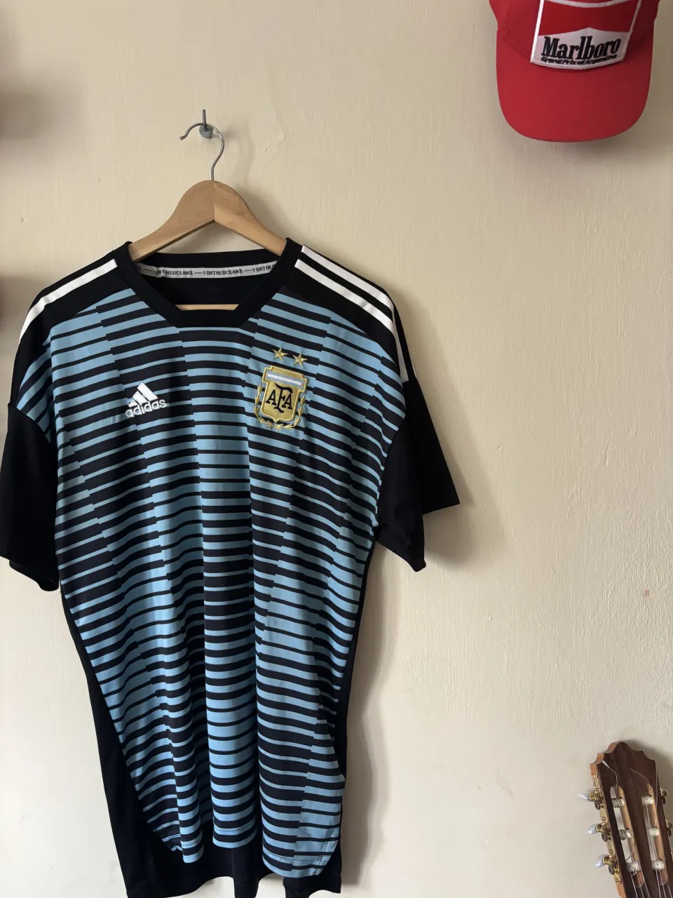 Remera deportiva de la Selección Argentina de fútbol. Diseño a rayas celestes y negras con detalles blancos en los hombros. Logo de Adidas y escudo de la AFA estampados. Tiene dos agujeritos que apenas ae notan