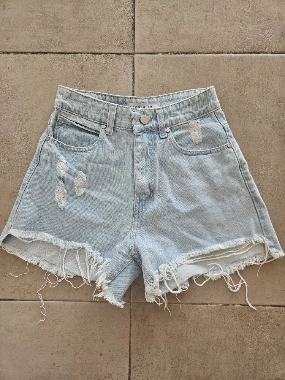 Short de jean celeste con roturas y flecos en el borde. Tiro alto, ideal para un look casual y moderno. Medidas con prenda apoyada: Cintura 30cm, Tiro 28cm, Cadera 45 cm aprox, Largo 30cm