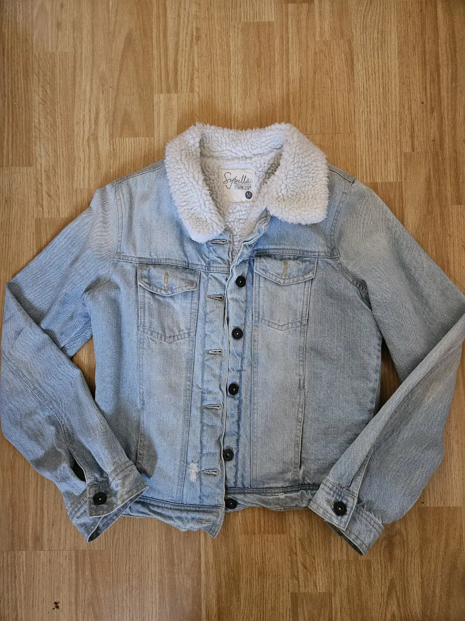 Campera de jean celeste con corderito blanco. Posee cuatro bolsillos delanteros. Detalles en la manga izquierda. Medidas: hombros 38cm, sisa  46cm, largo 53cm, magas 62cm.