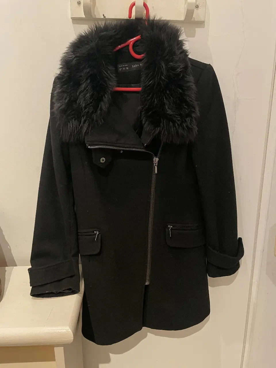 Tapado negro de mujer con cuello de piel sintética, cierre asimétrico con cremallera y bolsillos. Ideal para el invierno, estilo elegante y moderno.
