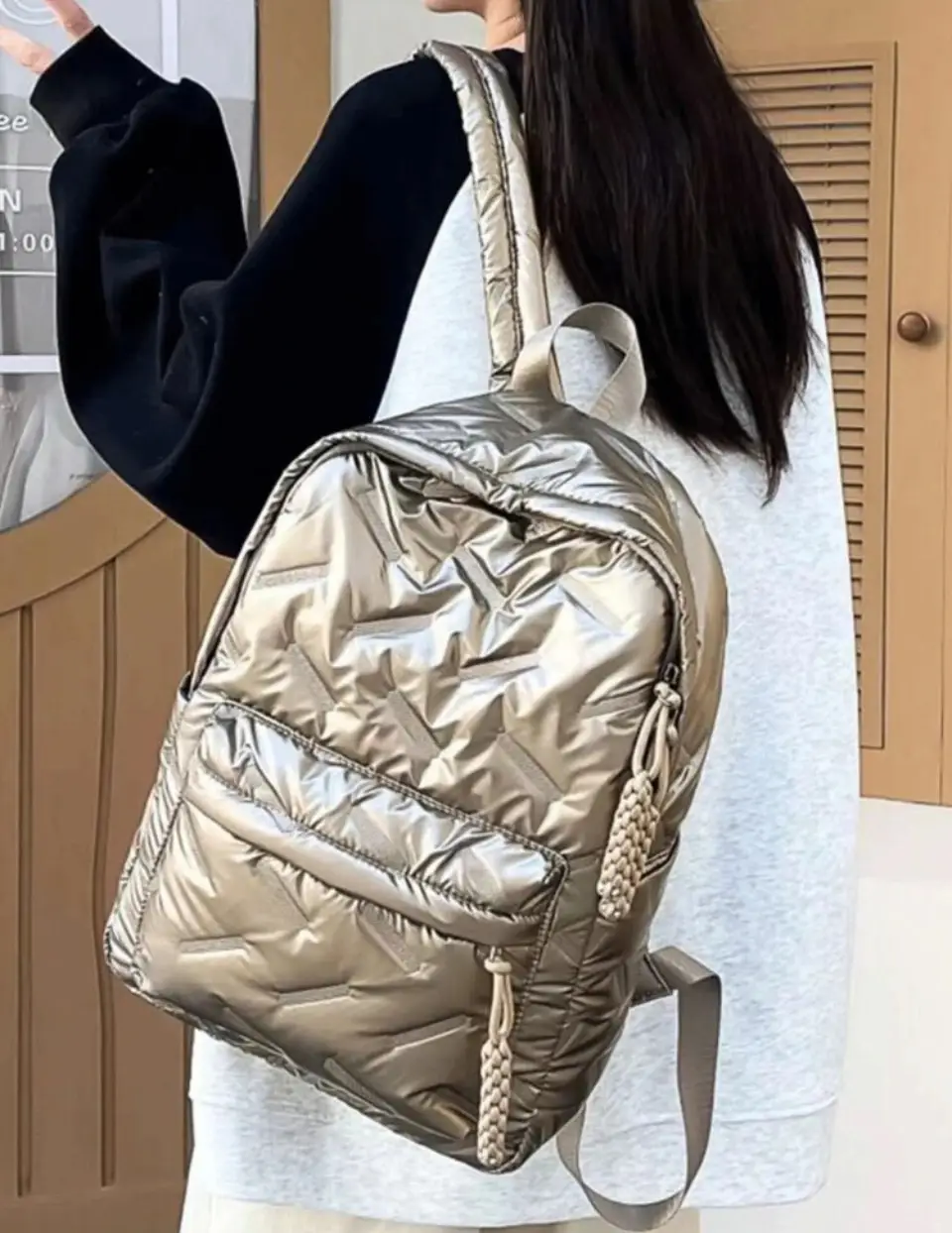 Mochila plateada acolchada con diseño geométrico. Ideal para uso diario, con bolsillo frontal y detalles trenzados en los cierres. Perfecta para un look moderno y funcional.