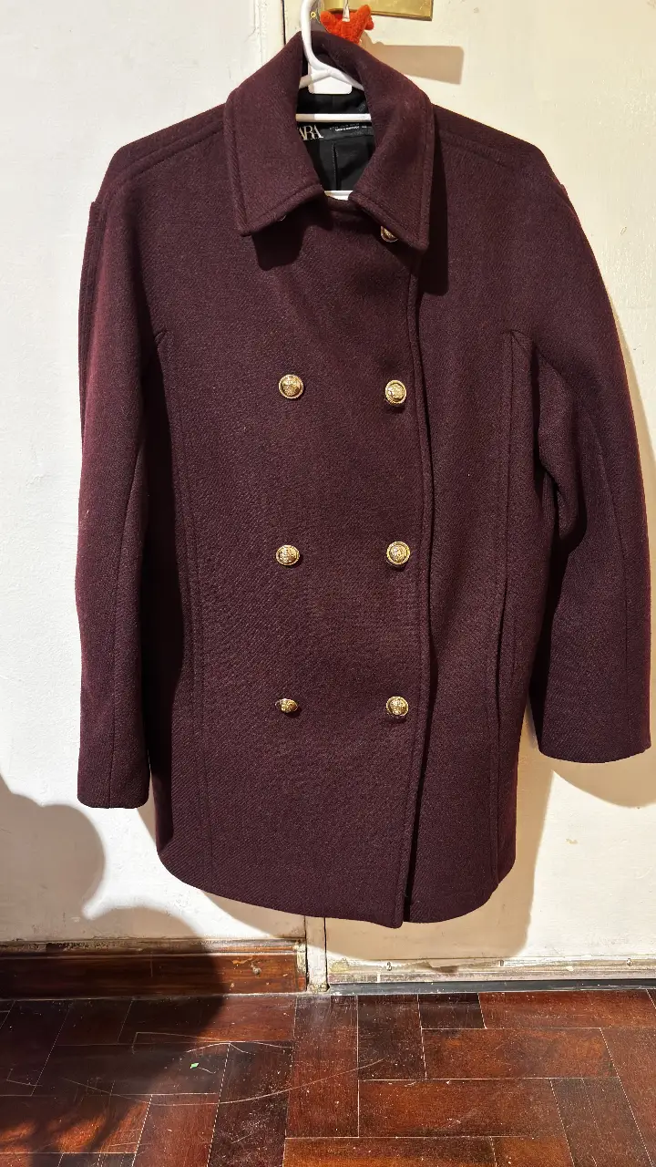 Tapado de paño color bordó de la marca Zara, con botones dorados. Ideal para el invierno, este abrigo combina elegancia y abrigo. Corte amplio debería ser S. Color bordó 