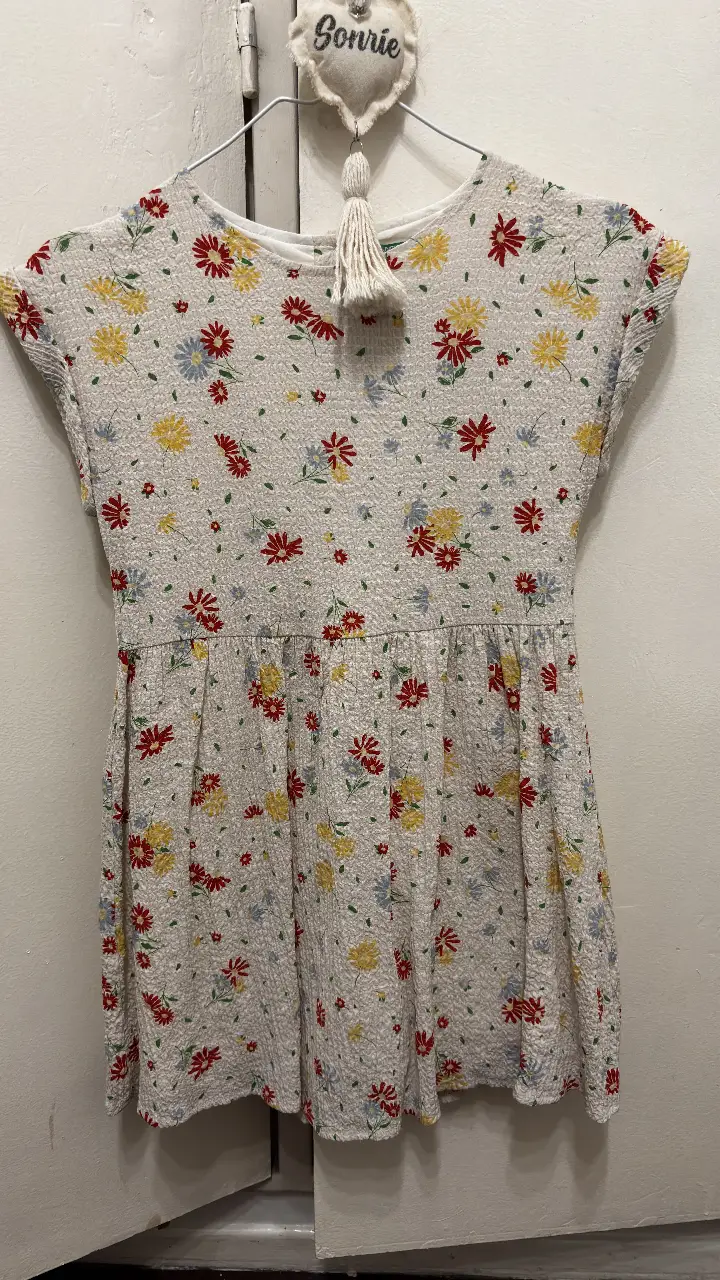 Vestido de niña, con estampado floral en tonos rojos, amarillos y azules sobre fondo blanco. Diseño con corte en la cintura y botones en la espalda. Marca United Colors of Benetton.