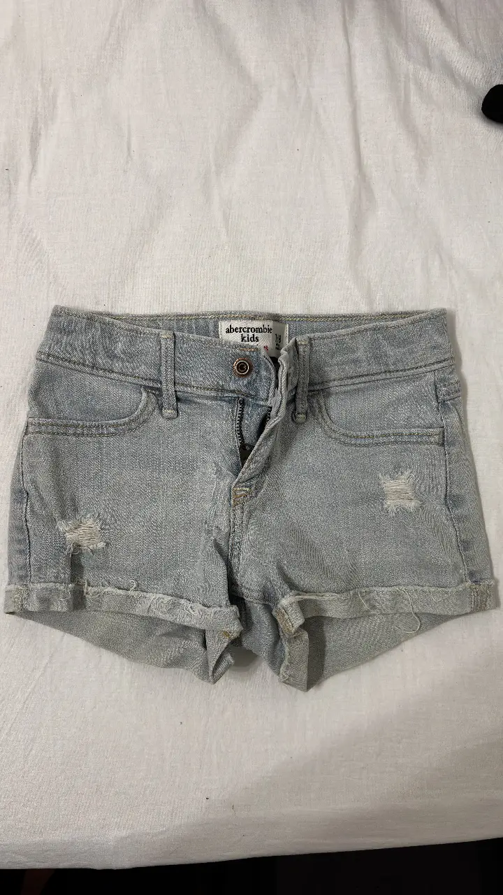 Short de jean Abercrombie Kids para niña, talle 7/8. Con detalles de roturas y dobladillo deshilachado. Ideal para un look casual y cómodo.