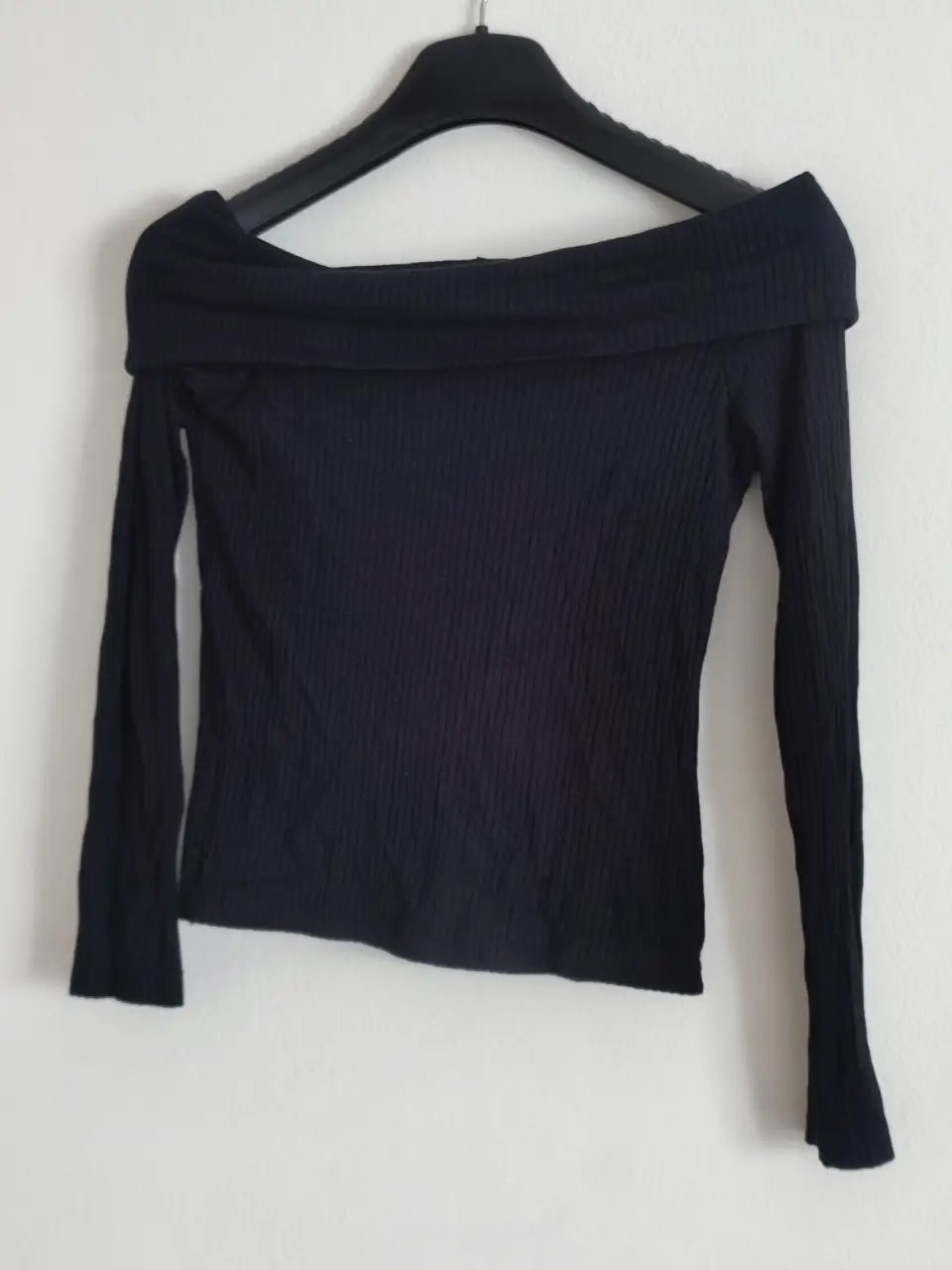 Remera de manga larga para mujer, de color negro, con cuello bote y tejido acanalado. Ideal para un look casual y elegante.