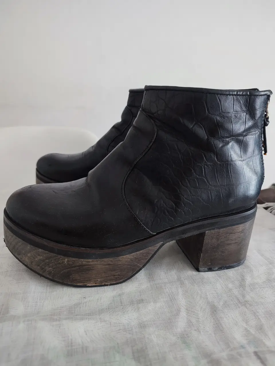 Botines negros de cuero con plataforma de madera. Diseño con textura de reptil en la caña y cierre trasero. Ideales para un look moderno y con estilo.