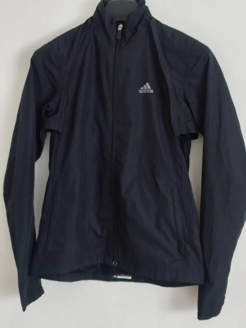 Campera deportiva mangas desmontables Adidas negra, ideal para running o actividades al aire libre. Con cierre completo y logo de la marca en el pecho. Diseño funcional y cómodo.