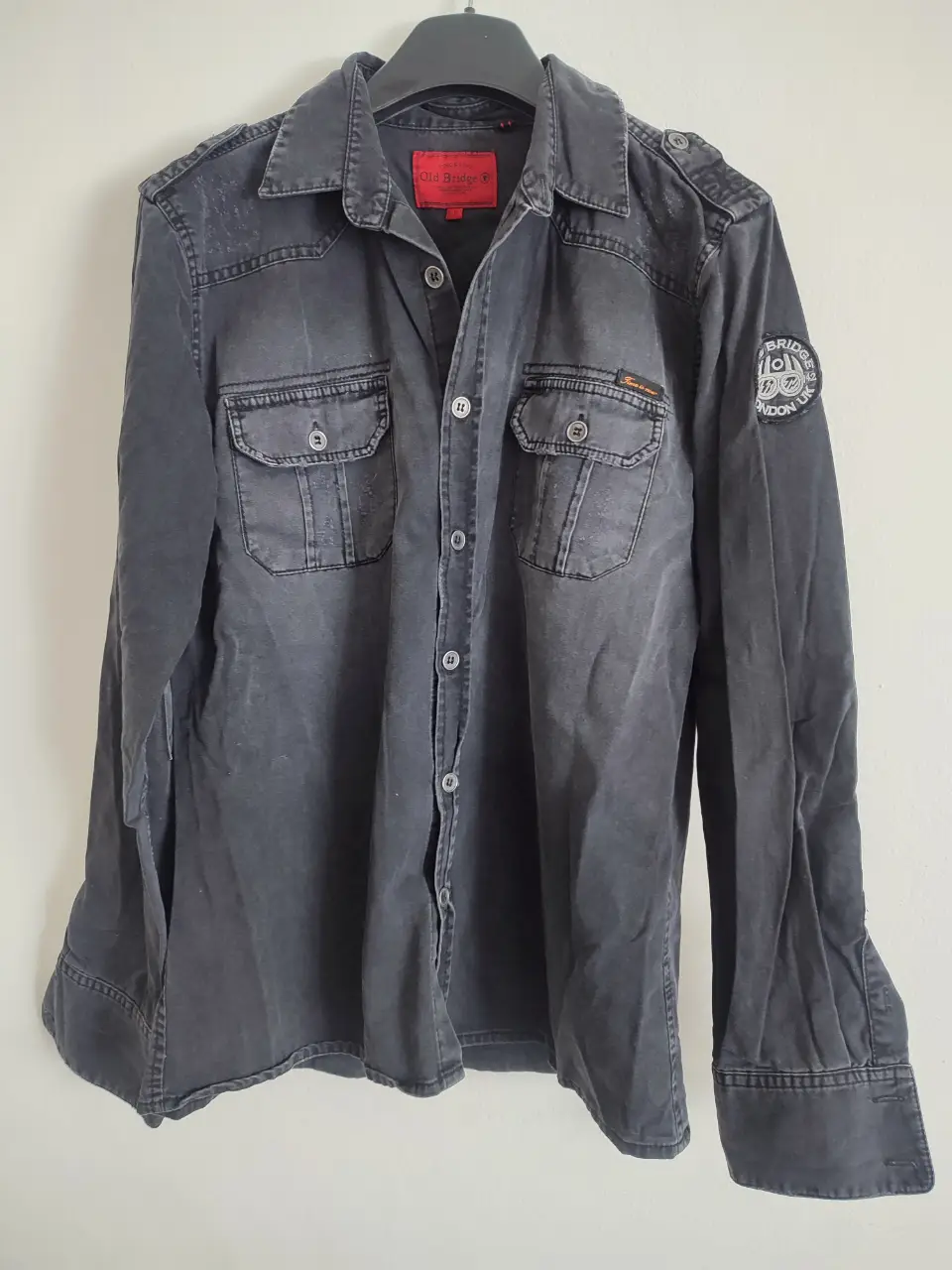 Camisa Old Bridge de hombre, de jean manga larga, color gris desgastado, con dos bolsillos delanteros y detalles de parches. Talle L.
