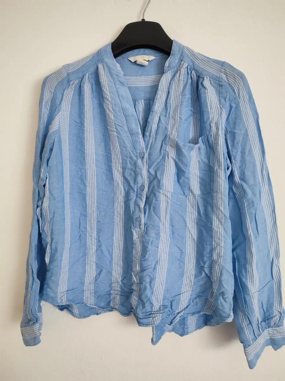 Camisa de mujer a rayas celeste y blanca, con cuello en V y un bolsillo en el pecho. Ideal para un look casual y fresco.