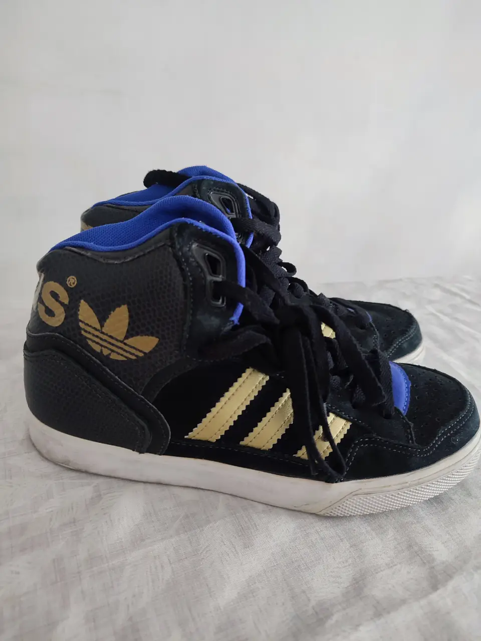 Zapatillas Adidas de caña alta en color negro con detalles dorados y azul. Ideales para un look urbano y deportivo.