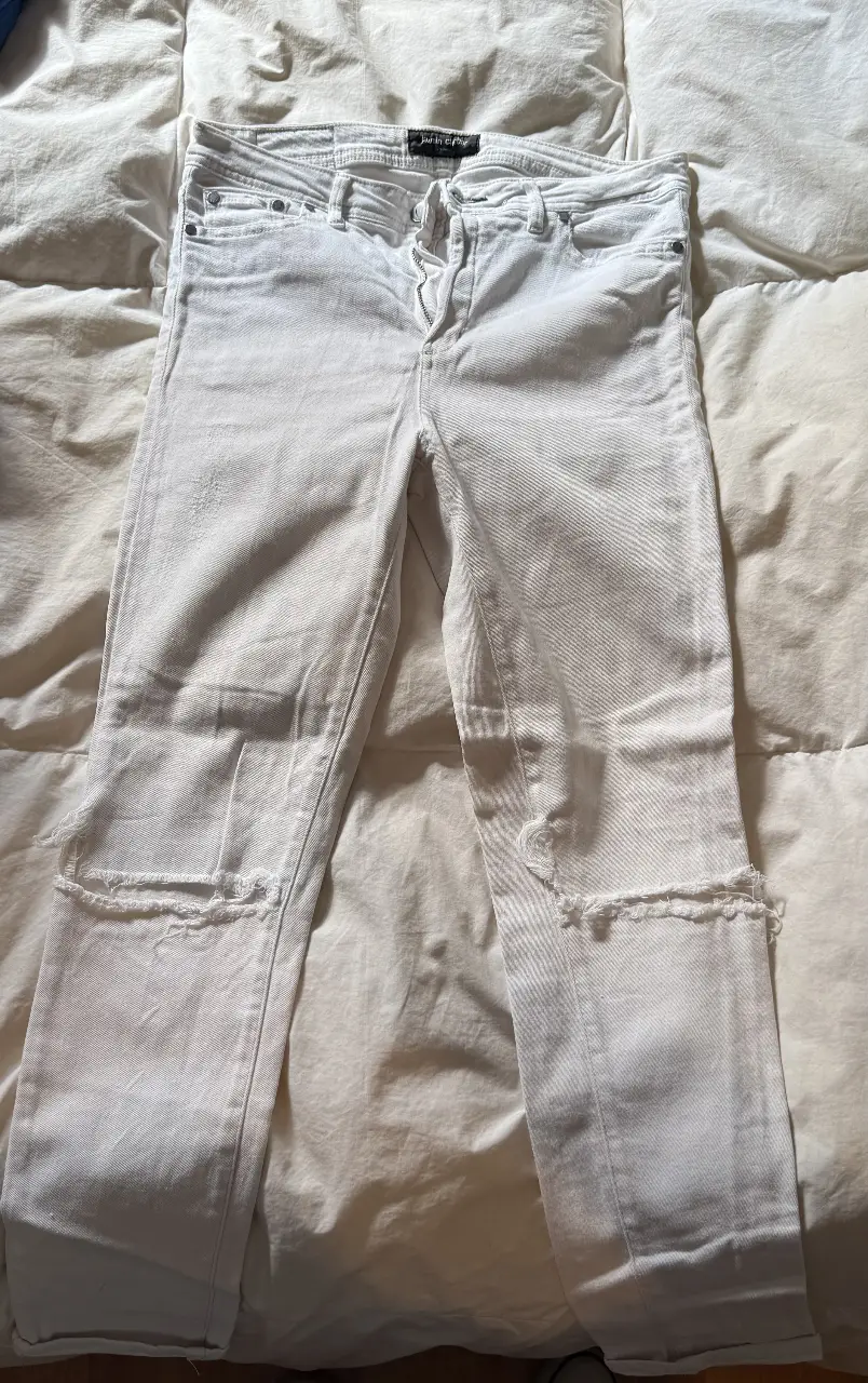 Jeans rectos blancos con detalles de roturas en las rodillas. Tiro medio. Ideal para un look casual y moderno.
