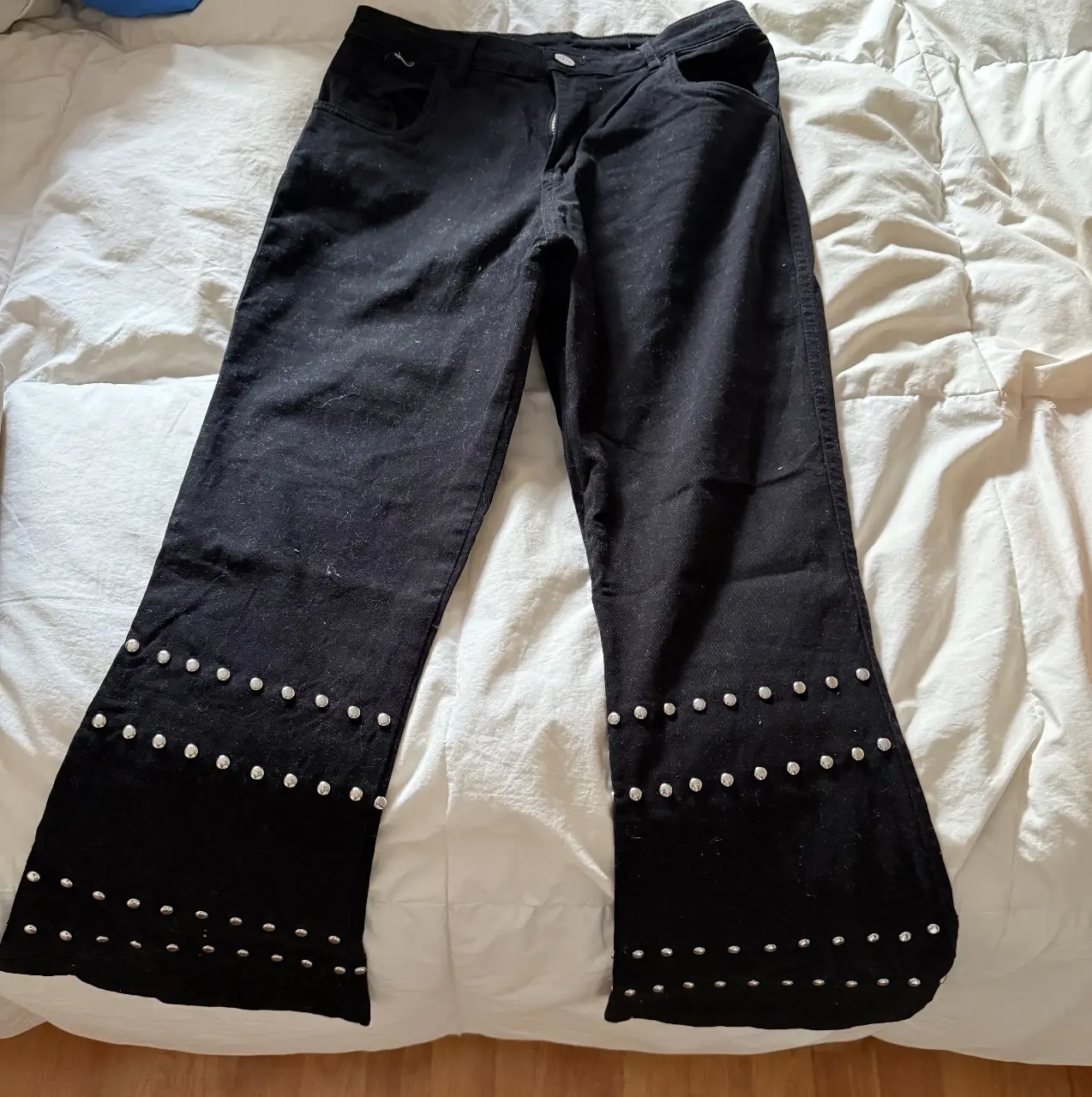 Pantalón de jean negro con diseño de tachas en el borde inferior. Corte recto y estilo Y2K.