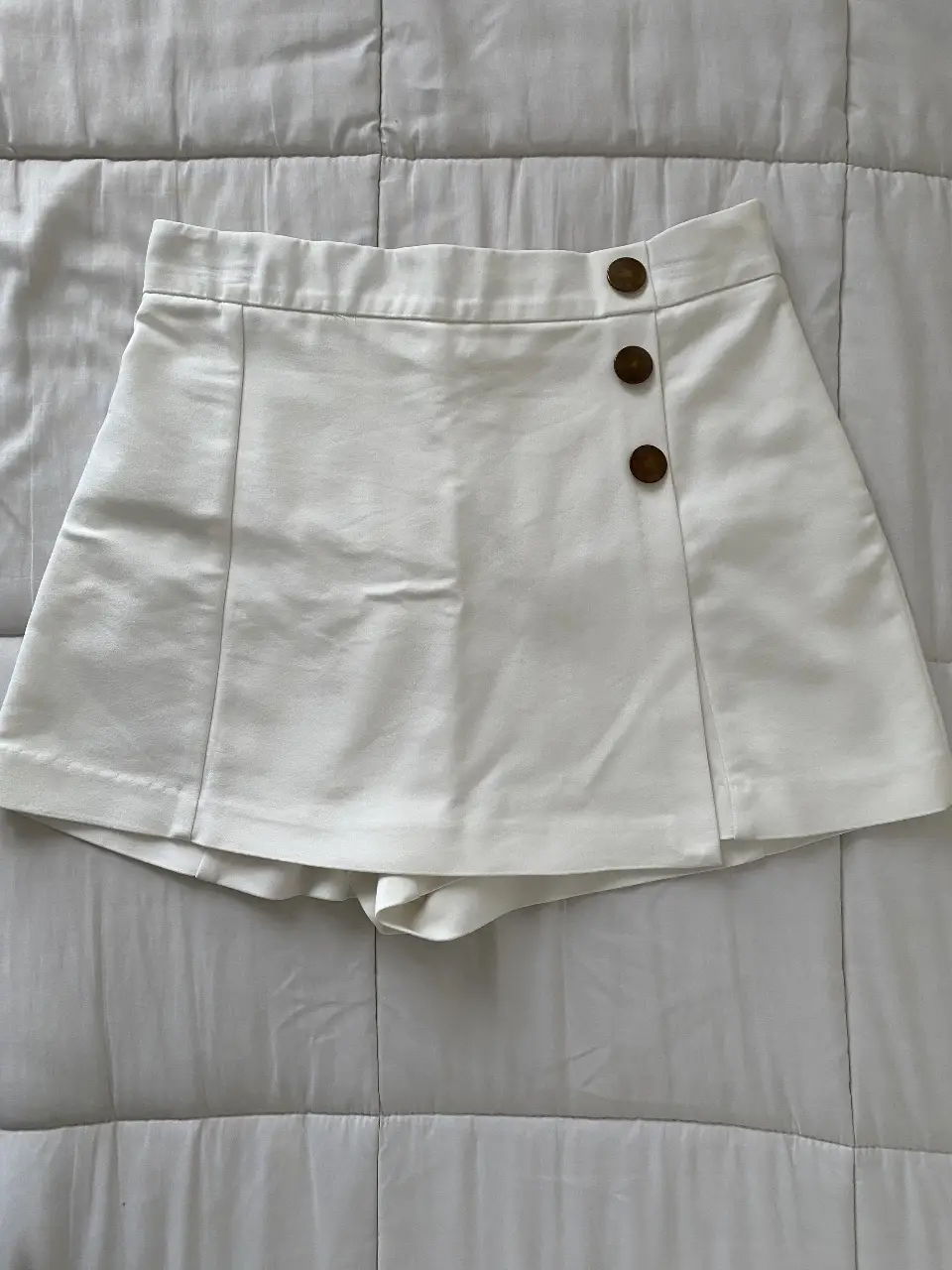 Skort blanco de Zara tiro alto con botones bronce. Ideal para un look fresco y moderno.