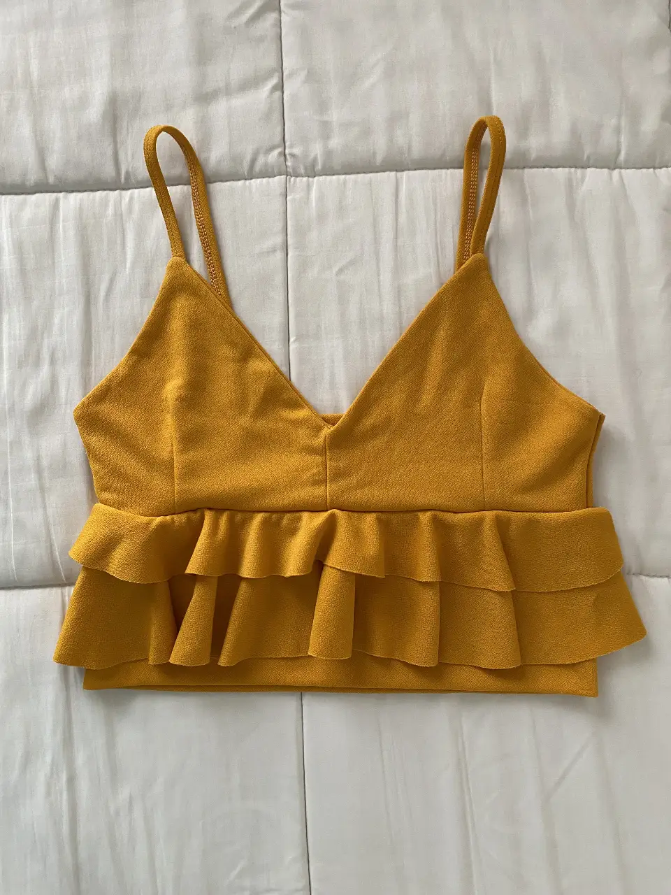 Top amarillo mostaza con volados en la parte inferior. Ideal para un look fresco y moderno. Perfecto para combinar con jeans o faldas.