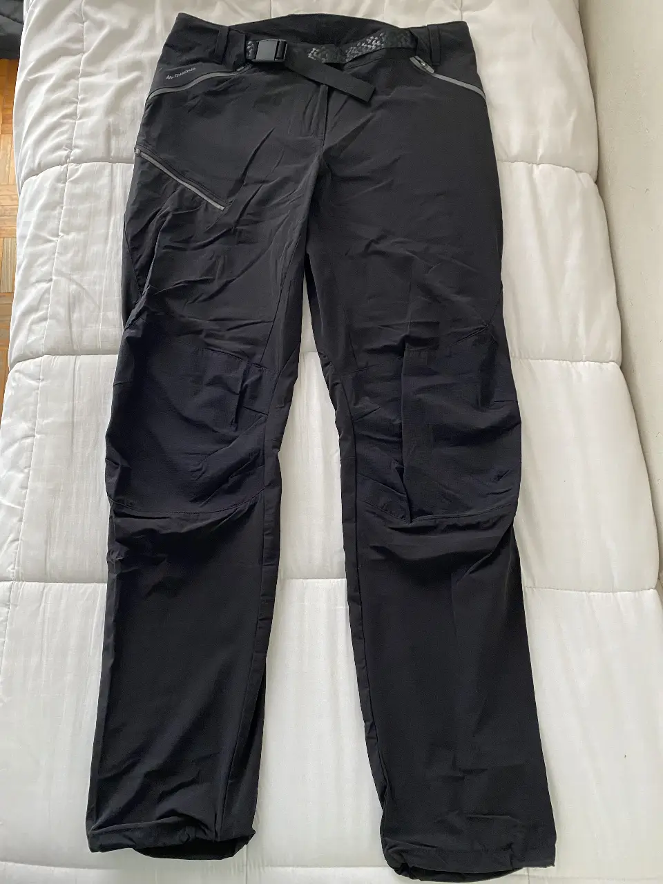 Pantalón de trekking negro rompevientos, con detalles en gris. Posee cinturón incorporado y bolsillos con cierre. Ideal para actividades al aire libre.