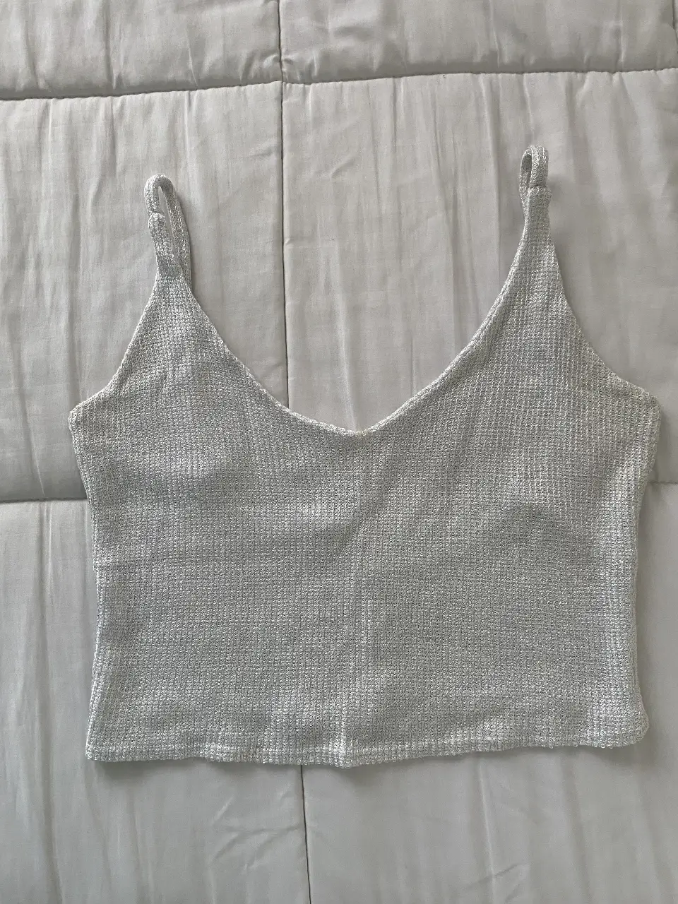 Top tejido de color blanco plateado, con breteles finos y escote en V. Ideal para un look casual y fresco.