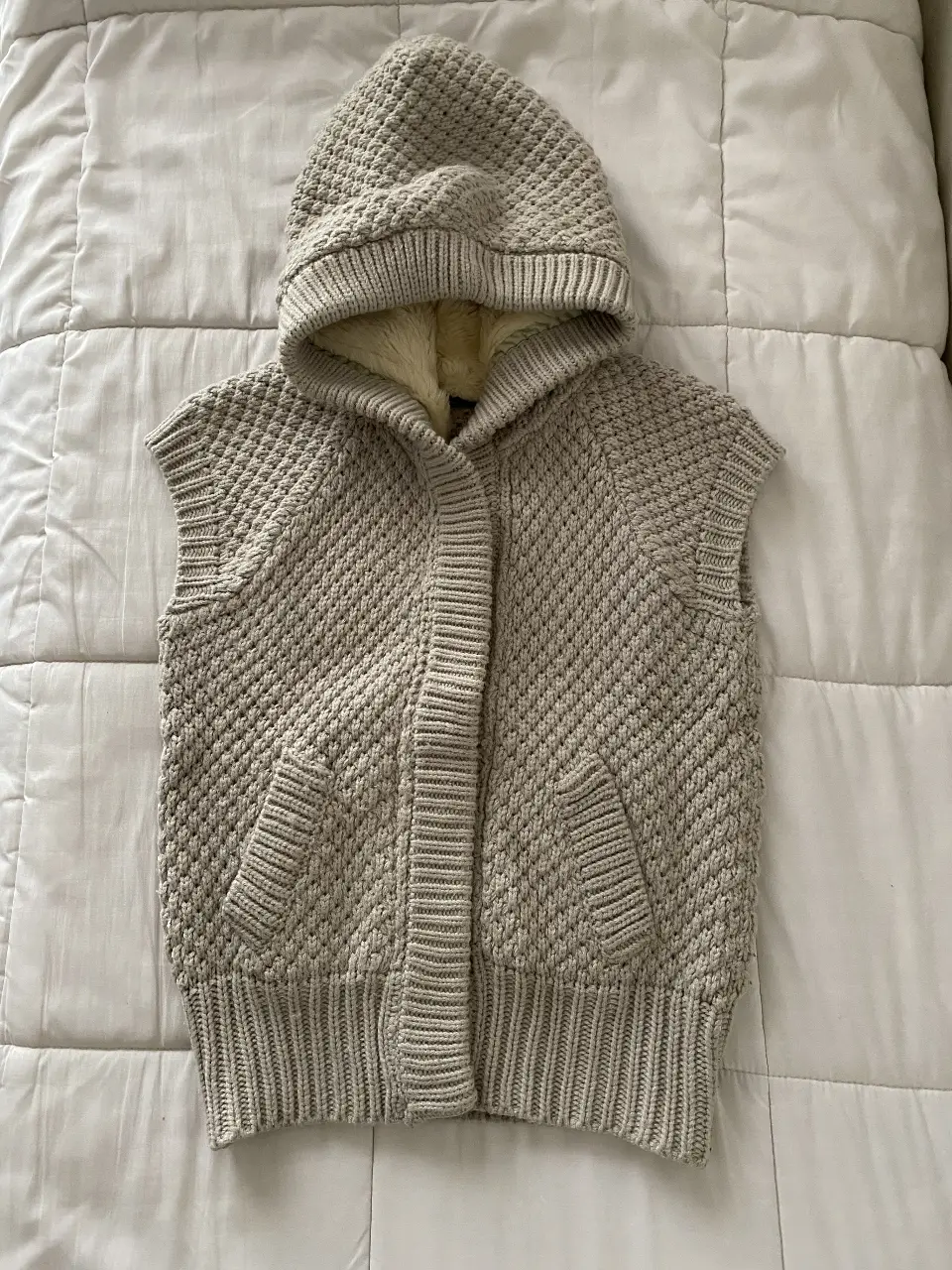 Chaleco tejido con capucha y forro de piel sintética. Posee bolsillos delanteros y cierre con botones. Ideal para un look casual y abrigado.
