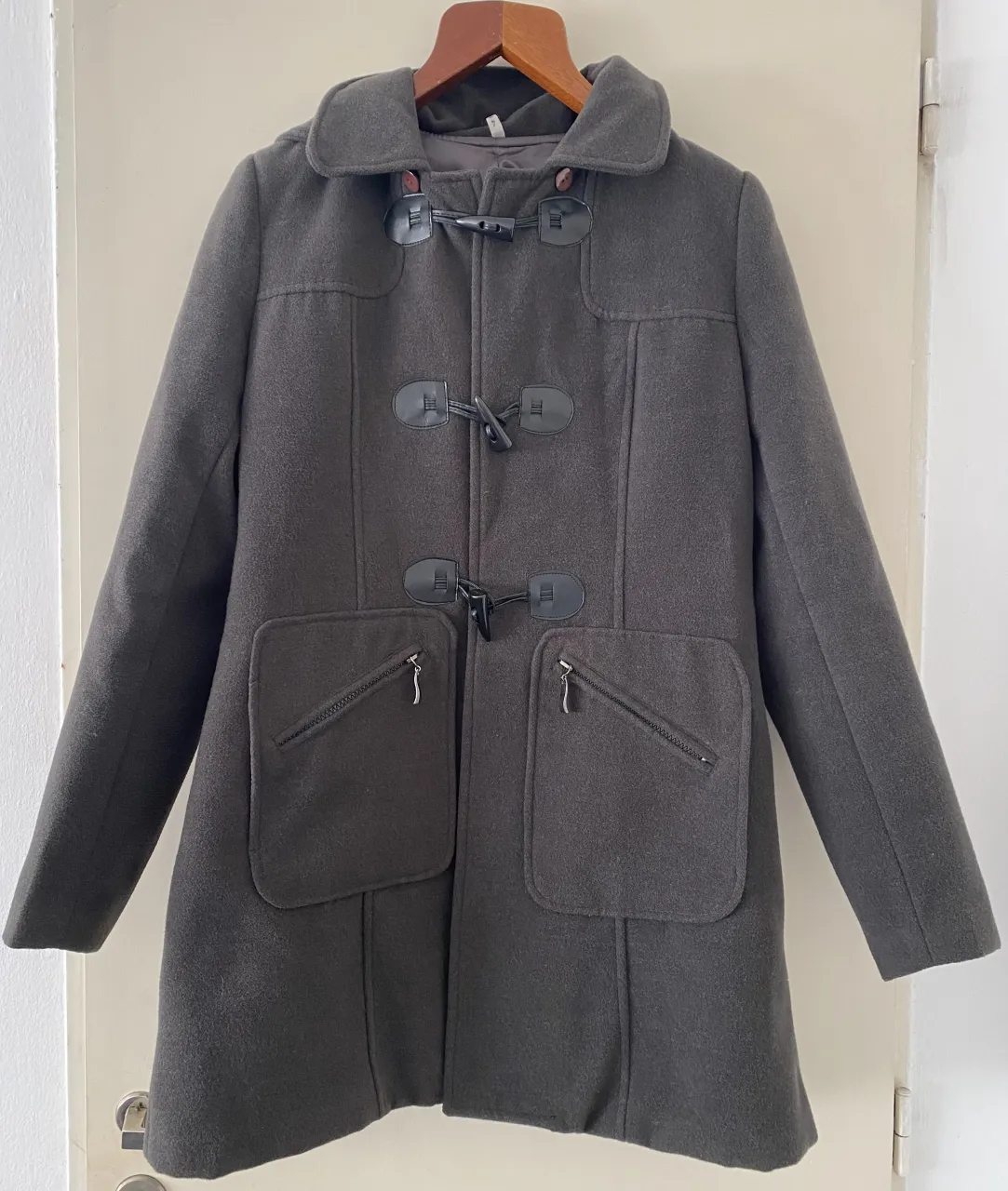 Abrigo de paño con capucha NUEVO, ideal para los días fríos. Posee detalles de botones y cierres en los bolsillos frontales. Su diseño clásico lo hace perfecto para combinar con cualquier outfit.